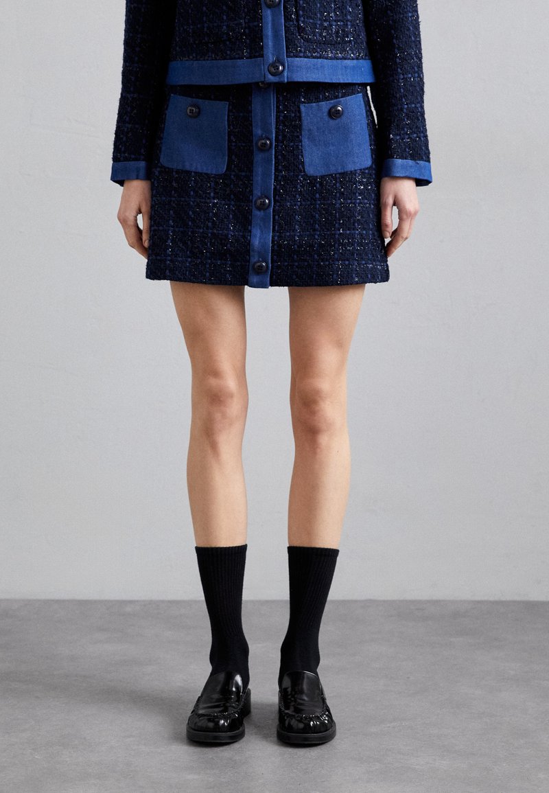Mornarica tweed jakna in krilo s sinimi akcenti na žepih in gumbnih zaprtjih. V kombinaciji s črnimi reberčnimi nogavicami in loaferji.