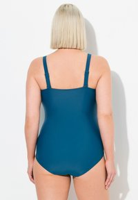 Maillot de bain une pièce teal avec bretelles réglables, texture lisse et coupe modeste. La vue de dos montre une silhouette ajustée et une finition sans couture.