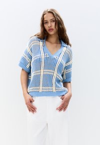 Lyseblå strikket sweater med løs pasform, korte ærmer og V-hals, prydet med cremede ternede mønstre.