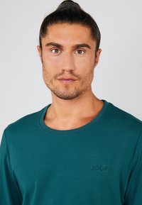Teal langærmet t-shirt lavet af bomuld, med rund halsudskæring og et lille broderet "JOOP!" logo på brystet. Glat tekstur.