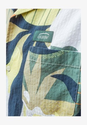Chemise à manches courtes avec poche plaquée, fabriquée en tissu texturé présentant un motif floral abstrait multicolore dans des tons de vert, jaune et bleu marine.