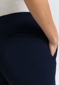 I pantaloni blu navy presentano un design slim con una tasca posteriore e cuciture laterali, realizzati in un tessuto liscio e elasticizzato per comfort e aderenza.