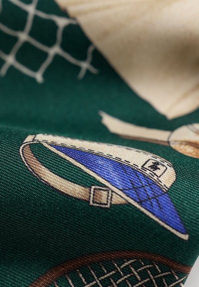 Gros plan d'un tissu avec équipement de tennis imprimé, comprenant une visière avec une visière bleue et une bride beige sur un fond vert foncé.