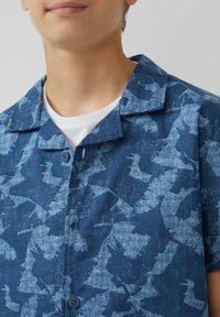 Kurzarmhemd aus navyblauem Stoff mit einem dezenten abstrakten Muster, einem spitzen Kragen und zwei Knopfverschlüssen an der Vorderseite.