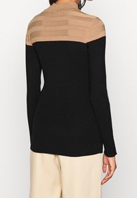 Sweter w prążki w kolorze czarnym z beżowym paskowanym wzorem na ramionach. Charakteryzuje się dopasowaną sylwetką i okrągłym dekoltem.