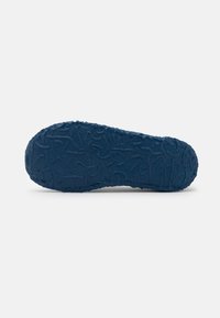 Sole of a shoe, textured rubber in dark blue, featuring a wavy pattern with uneven ridges for grip and traction.