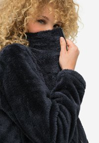 Mörkblå konstpälsjacka med hög krage, blixtlås och strukturerad yta med mjukt, fluffigt tyg, perfekt för att hålla värmen.