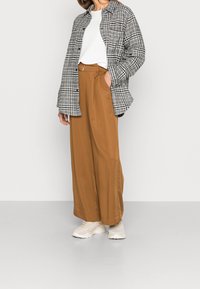 Gray and white plaid oversized jacket over a white top, paired with wide brown trousers and light-colored sneakers. Soft textures, relaxed fit.