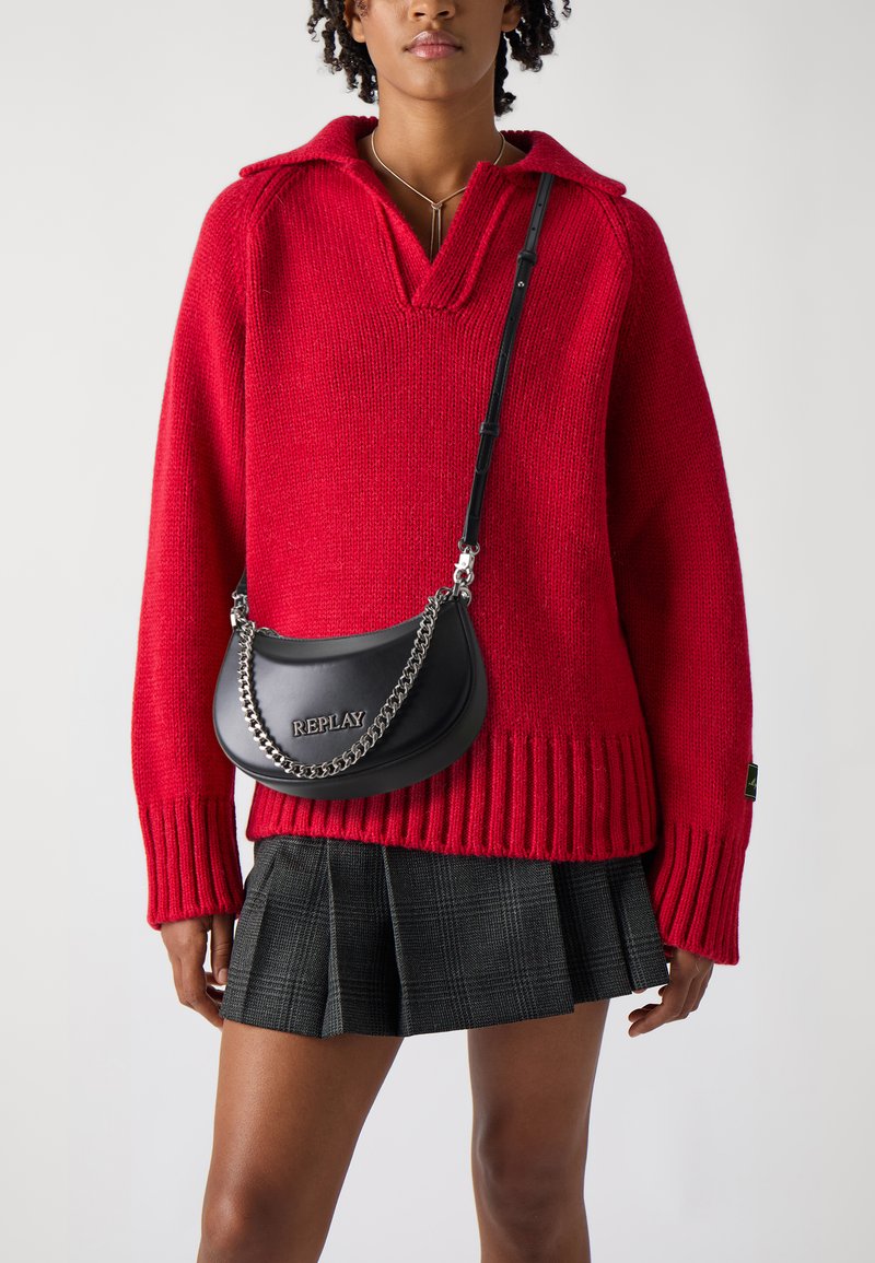 Suéter de punto rojo con cuello, combinado con una falda negra con pliegues y un pequeño bolso negro con cadena y logotipo.