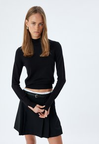Maglione aderente nero con collo a imbuto abbinato a una gonna nera a vita alta, dotata di una cintura piatta e pieghe sottili. Tessuto texturizzato con maniche lunghe.