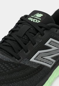 Mustad musta New Balance EvoZ tossud rohelise tallaga, mustade paeltega ja peegeldava "N" logoga küljel, näidates lähedalt keele ja ülemise osa detaili.