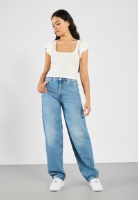 Hvit ribbet topp med firkantet hals og korte volangermner, sammen med lyseblå vide jeans og hvite sneakers.