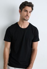 T-shirt en coton noir avec un col rond et des manches courtes. Design légèrement ajusté avec un petit logo sur l'ourlet. Texture lisse.
