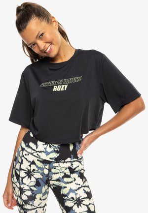 Black cropped t-shirt with "ACTIVE BY NATURE ROXY" in light green text. Paired with patterned leggings featuring floral designs in pale and dark colors.