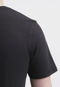 Camiseta de algodón negra con cuello redondo y mangas cortas, con un diseño liso y textura suave, vista desde la parte de atrás.