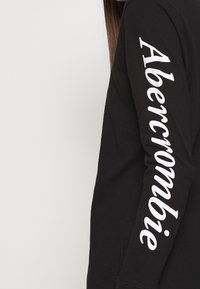 Zwarte longsleeve shirt met "Abercrombie" in witte letters verticaal langs de rechtermouw. Gemaakt van zachte stof met een fitted ontwerp.