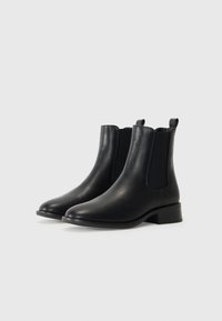 Botas Chelsea de cuero negro con paneles laterales elásticos, punteras redondeadas y un tacón bajo tipo bloque. Presentan tiradores para facilitar su colocación.