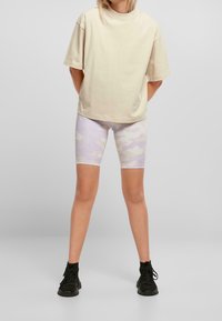 Světle béžové oversized tričko, doplněné pastelově fialovými maskáčovými cyklistickými šortkami. Černé kotníkové boty dotvářejí tento outfit. Jednoduchý, ležérní design.