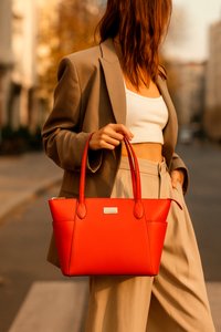 Rode handtas van glad materiaal, met dubbele handgrepen, een rechthoekige vorm en een zilveren logo accent aan de voorkant.