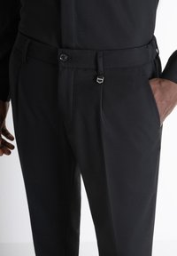 Pantaloni neri realizzati in tessuto testurizzato, con chiusura a bottone, passanti per cintura regolabili e tasche laterali. Design semplice e sartoriale.