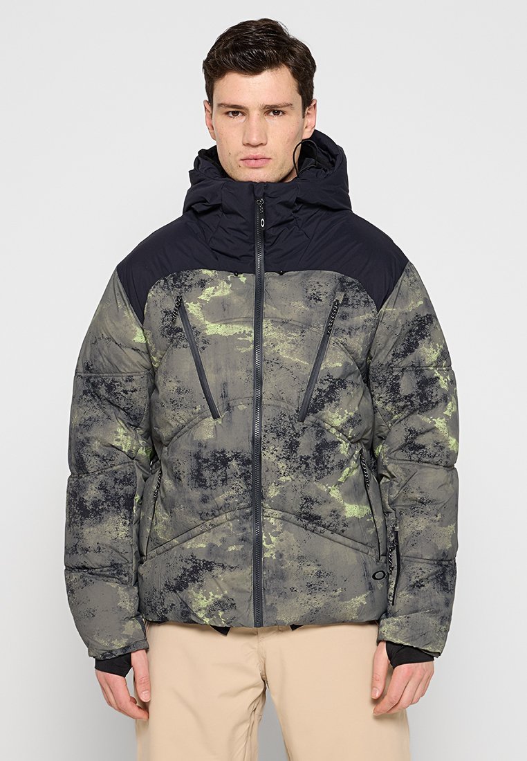 Doudoune avec capuche, présentant un imprimé camouflage dans des nuances de gris et de vert, et des poches zippées à l'avant. Tissu texturé.