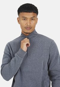 Felpa grigia con zip e colletto alto, polsini a costine. Realizzata in tessuto morbido, presenta una zip corta e una texture minima.