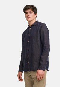 Camicia button-up in lino navy con colletto, caratterizzata da bottoni in legno e un logo ricamato discreto sul petto. Maniche lunghe con polsini.