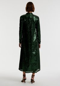 Groene pailletten jurk met lange mouwen en een hoge hals, met een rechte silhout en een lengte tot halverwege de kuit. Achteraanzicht weergegeven.