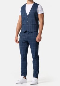Marineblauw geruit pak met een getailleerd vest en taps toelopende broek, aangevuld met witte sneakers, die een moderne, op maat gemaakte uitstraling laten zien.