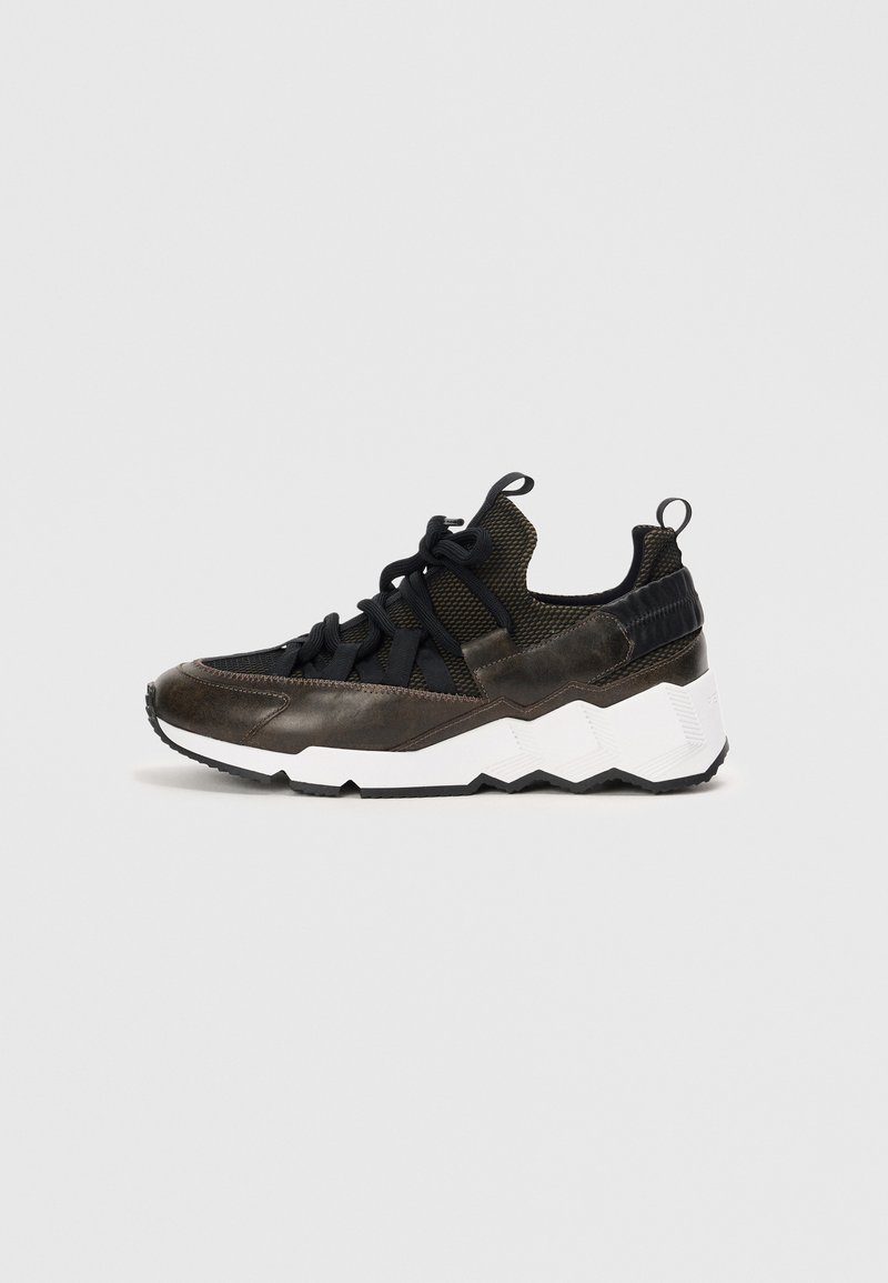 Zapatillas marrones y negras con una parte superior texturizada, un sistema de cordones prominente y una suela blanca con zigzag y una suela negra rugosa.