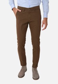 Pantaloni marroni slim-fit in cotone, dotati di tasche frontali, vita con bottone e una texture liscia, abbinati a scarpe in suede grigie.