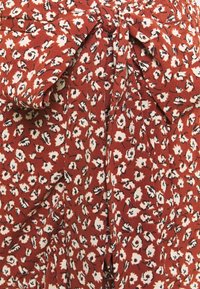 Tissu rouge à motifs floraux avec des accents blancs et noirs. Comprend une taille nouée, une texture douce et des détails de design plissés.