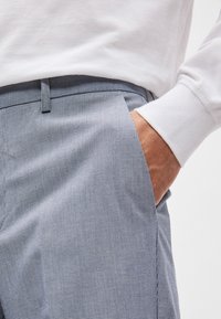 Γκρι και λευκό καρό παντελόνι με ίσια γραμμή, διαθέτοντας πλευρικές τσέπες και επίπεδο μπροστινό μέρος, σε συνδυασμό με λευκό μακρυμάνικο μπλουζάκι.