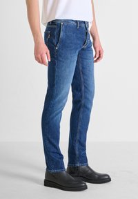 Blue denim jeans featuring a slim fit design, five pockets, and visible stitching details. Paired with black leather ankle boots.