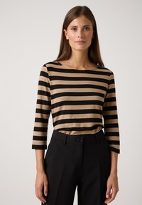 Gestreiftes Langarmoberteil in Beige und Schwarz mit rundem Ausschnitt. Kombiniert mit maßgeschneiderten schwarzen Hosen, die eine glatte Textur aufweisen.