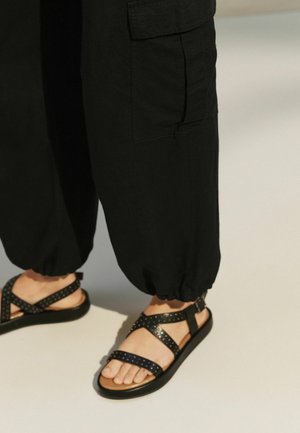 Pantaloni cargo negri, ușori, cu manșete elastice, asortați cu sandale negre cu curele încrucișate și accente cu tinte.