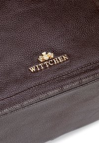 Sac en cuir marron avec une surface texturée, arborant un logo doré "Wittchen" et des coutures précises le long des bords.