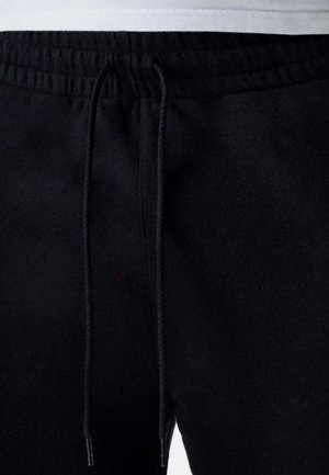 Schwarze Sweatpants aus weichem Stoff mit einem elastischen Bund und Kordelzug, sichtbaren Nähten und ohne Taschen.
