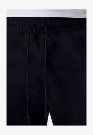 Zwarte joggingsbroek van zacht materiaal met een elastische tailleband en een trekkoord, zichtbare stiksels en zonder zakken.