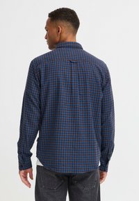 Langarmshirt in donkerbruin en blauw plaidpatroon, met een standaardkraag en knopenmanchetten, een afgeronde zoom en rugdeel-detail.