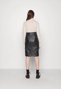 Zwarte leren rok met een aansluitend ontwerp, voorzien van een achterrits en een lengte tot de knie. Draag het met een lichtbeige trui en zwarte schoenen.