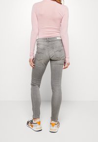 Gray skinny jeans with a high waist, back pockets featuring decorative seams, paired with a light pink long-sleeve top and multicolor sneakers.