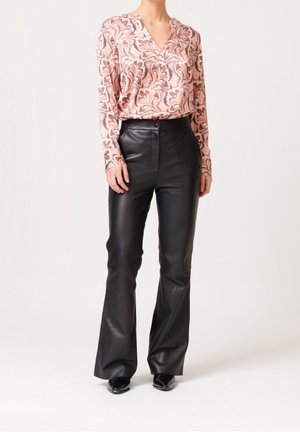 Langärmliges rosa Oberteil mit Paisleymuster, kombiniert mit schwarzen Lederflare-Hosen. Das Outfit hat einen V-Ausschnitt und eine schmale Passform.