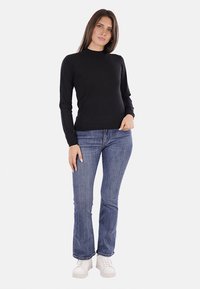 Maglia nera a maniche lunghe con colletto alto, abbinata a jeans blu a zampa d'elefante e sneakers bianche. Il tessuto sembra liscio e aderente.