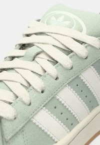 Light green suede sneaker with white accents, textured laces, and three white stripes. Features perforations and a circular logo on the tongue.