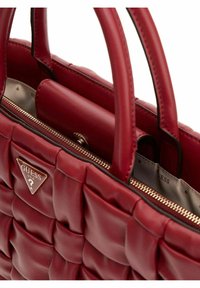 Sac à main en cuir matelassé rouge avec deux poignées, fermeture éclair et un logo en métal triangulaire. L'intérieur présente une doublure lisse et des poches.