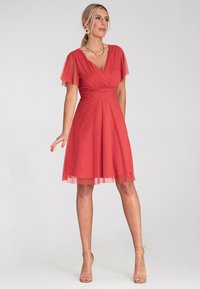 Rotes Kleid mit enger Passform am Oberteil und weit schwingendem Rock. Mit kurzen, durchsichtigen Ärmeln und einem V-Ausschnitt. Glatte Stoffoberfläche mit mehrlagigem Saum.