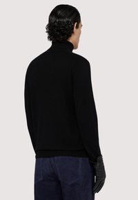 Svart polotröja med en åtsittande design, stickad textur och ribbad fåll. Bärs med mörkblå mockabyxor och svarta läderhandskar.