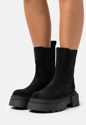 Stivaletti neri in suede con suola in gomma spessa, dotati di pannelli laterali elastici e una finitura liscia. Sopracchio testurizzato con cuciture semplici.