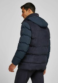 Marine blauwe pufferjack met een gestructureerde suède afwerking, voorzien van een afneembare capuchon, elastische manchetten en gestikte panelen.